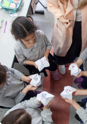 Cinco alunas brincando com folhas de papel.